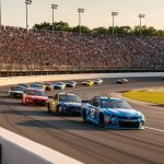 “Packed grandstands and stock cars racing through a left-hand turn at North Wilkesboro Speedway during NASCAR return event day”