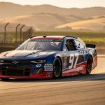 Shane Van Gisbergen’s Trackhouse No. 97 NASCAR stock car drives through a Sonoma Raceway road-course corner with sunlight and vine-covered hills in the background.