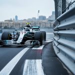 Formula 1 car speeding through a tight corner on the Baku City Circuit beside track barriers with a softly blurred city skyline in the background.