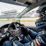 Christopher Bell in the No. 20 Toyota Camry cockpit, steering through Canadian Tire Motorsport Park with the track and grandstands softly blurred behind him.
