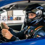 Zane Smith seated inside a Ford NASCAR cockpit in the garage, holding his steering wheel before a race.